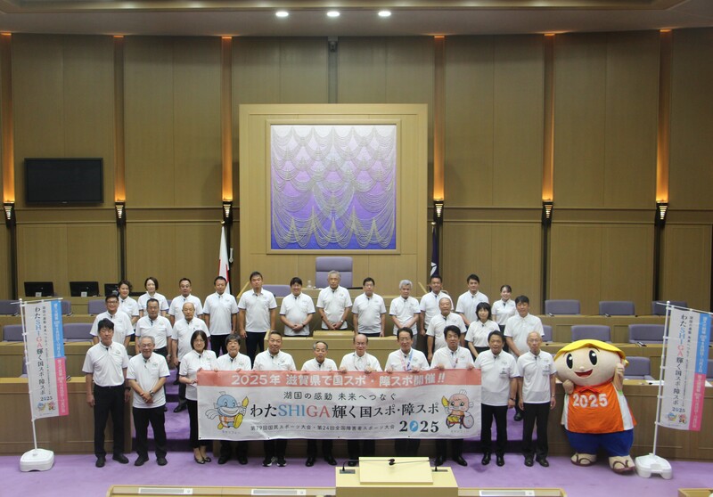 2025年開催のわたSHIGA輝く国スポ・障スポのポロシャツを着用した草津市議会議員とオレンジ色のスポーツ衣装を着たたび丸