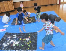 床上に広げたブルーシートの上でスポンジを投げるこどもたちの写真