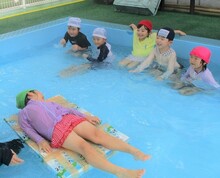 プールで、牛乳パックを組み合わせた板の上に乗る人の写真