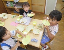 卓上の食器を手で持つこどもたちの写真