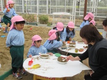 屋外のテーブルで食事のごっこ遊びをするこどもたち