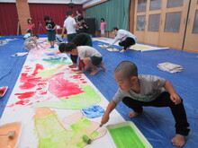 ロール紙の上で絵具をローラーで塗り広げるこどもたちの写真