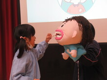 人形の歯に、歯ブラシをあてて磨くこどもの写真