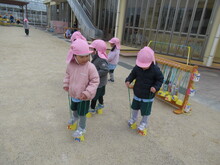 屋外でパカポコ（缶ぽっくり）をするこどもたちのようす