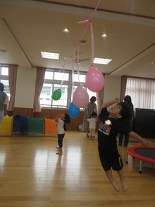 こどもたちが屋内で天井からつるした風船に向かってジャンプする様子