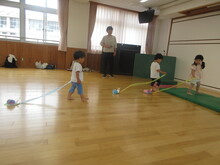 こどもたちが屋内でカタツムリの形をした工作物にロープをつけ、連れて歩き遊んでいる様子