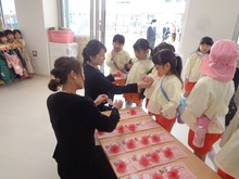 受付で担任が園児の胸にリボンを付けています。