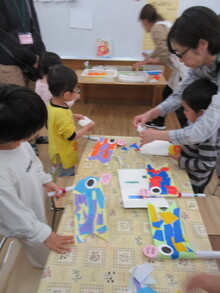 机の上で、色のついた紙を貼ってこいのぼりをつくっている親子