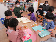 机の上でクリスマスのモチーフを色紙で作るこどもたち