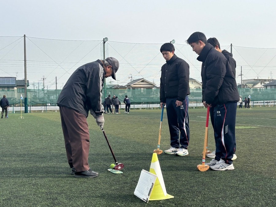 グラウンドゴルフを教える大人と、それを真剣に聞く高校生たちのようす