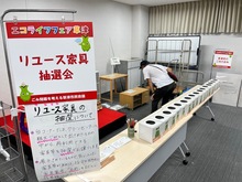 リユース家具抽選会の風景。ステージ上にリユース家具が並べられ、ステージしたのは抽選箱がおかれている。
