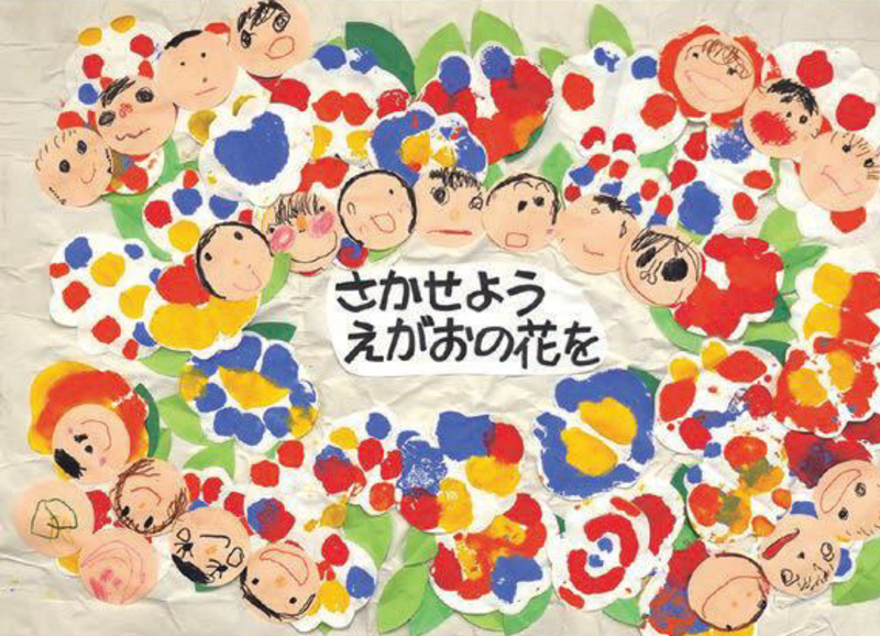 「さかせよう　えがおの花を」色とりどりの花と、たくさんの人々が文字を囲んでいる作品