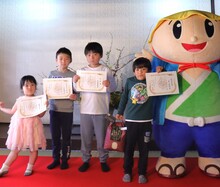 賞状をもった4人のこどもたちと「たび丸」が並んでいる記念写真