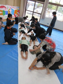 長いロール紙を広げ、その上に寝転がるこどもたちの写真