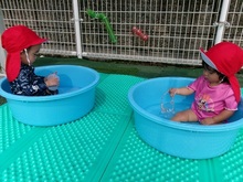 大きなたらいの水に入ってあそぶこどもたちの写真