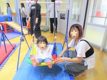 屋内でブランコに乗るこどもとそれを支える保護者の写真