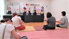 おはなし会にて、研究会の方々とそれを聞くこどもを抱えるおとなの背中が写った写真
