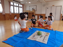 シートの上に置かれたスイカを囲むこどもたちの写真
