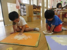 絵具のスタンプに掌を押し当てて、画用紙にぬりひろげています。