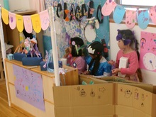 段ボールで作ったおしゃれショップのしつらえの後ろで、頭に様々なおしゃれグッズを付けたこどもたちが集っています。