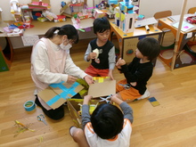 胃段ボールで家を作ろうと3人ではさみで段差をそろえようとしています。